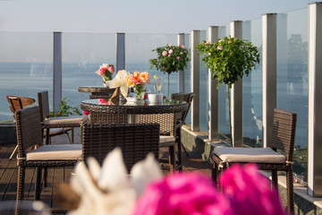 Outdoor cafe on the roof. A cozy wicker table with a glass top and decor with fresh roses in the outdoor cafe-bar on the roof of the hotel, in the morning, overlooking the sea and the sunrise.