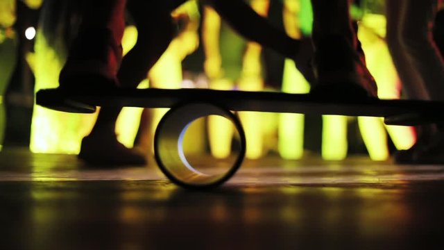 Close-up of man’s feet on skateboard. Young skater dancing on balance board at neon lighted nightclub.