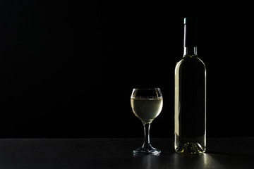 Wine bottle and glass with white wine on dark glossy background.