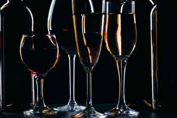 Bottles of wine and different glasses of wine on a dark background