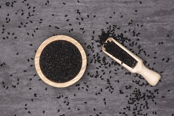 Lot of whole black cumin seeds with wooden scoop and wooden bowl flatlay on grey stone