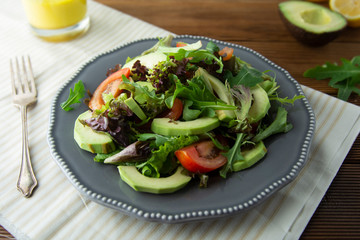 Healthy salad mix of iceberg, spinach, avocado and cucumber with olive oil, tomato and lemon.