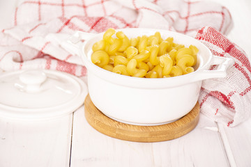 Lot of whole pasta cavatappi in a ceramic stewpan with a tea towel on white wood