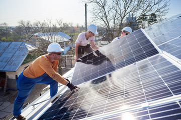 Male workers installing solar photovoltaic panel system. Electricians mounting blue solar module on...