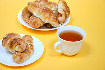 croissants on a white plate with a Cup of tea on a yellow background