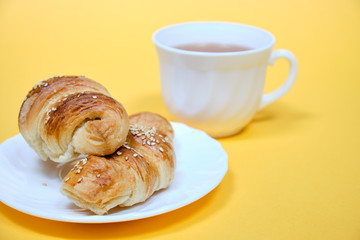 croissants on a white plate with a Cup of tea on a yellow background