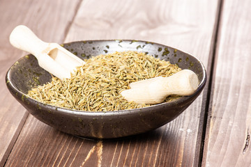 Lot of whole roman caraway seeds two wooden scoops in a grey ceramic bowl on brown wood