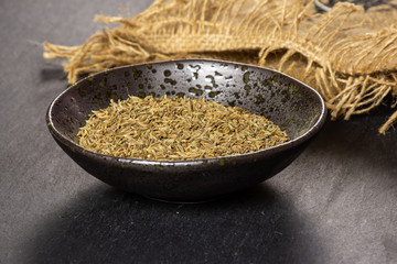 Lot of whole dry roman caraway seeds in a grey ceramic bowl on grey stone