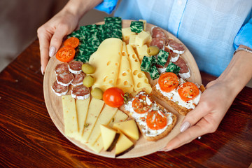 Close-up photo cheese plate - woman's hands cutting different kinds of cheeses in counter at kitchen home interior.