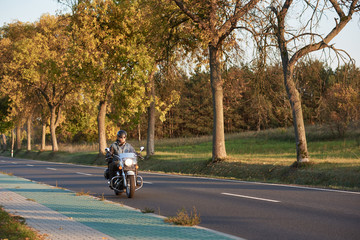 Bearded biker in sunglasses, helmet and black leather clothing riding cruiser powerful motorcycle...
