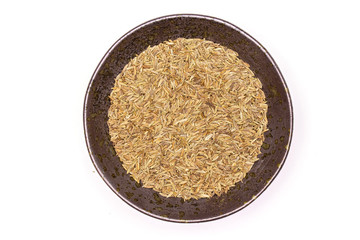 Lot of whole roman caraway seeds in a grey ceramic bowl flatlay isolated on white background