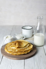 Pancakes on a white wooden table with milk and sour cream