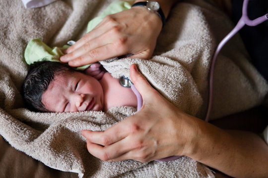 A new born baby was born at home in a home birth. Shortly after the birth a midwife checks all the vitals which is a new born screen, here she checks the heart rate.