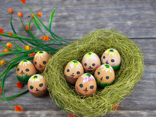 eggs with cute faces in a straw nest on a wooden background for Easter