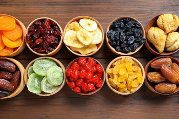 Bowls with different dried fruits on wooden background, flat lay. Healthy lifestyle
