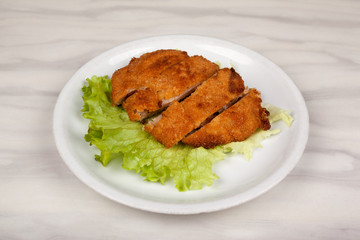 Fried meat cutlet in breadcrumbs sliced and green leaf lettuce.