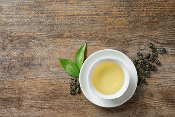 Cup of Tie Guan Yin oolong and tea leaves on wooden table, top view with space for text