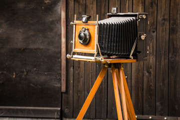 An old large format camera on a wooden tripod.