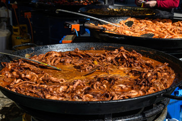 Fototapeta premium Octopus cooked with tomato sauce in a large traditional black fry pan at a street food festival, ready to eat seafood, side view