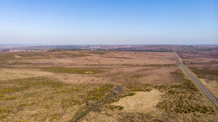 Aerial view of the New Forest National Park with heathland, road and waterway under a majestic blue sky.