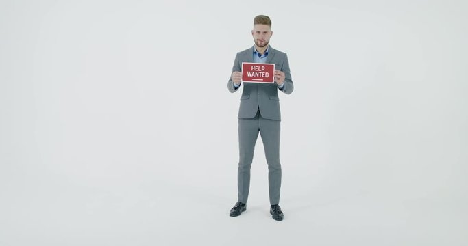 FIXED Handsome Caucasian HR manager wearing suit holding recruitment sign saying Help Wanted. Light grey background. 4K UHD