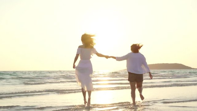 Young Asian lesbian couple running on beach. Beautiful women friends happy relax having fun on beach near sea when sunset in evening. Lifestyle lesbian couple travel on beach concept.