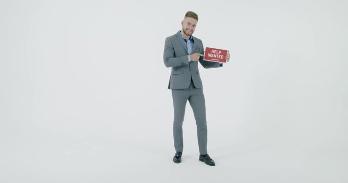 FIXED Handsome Caucasian HR manager wearing suit holding recruitment sign saying Help Wanted. Light grey background. 4K UHD