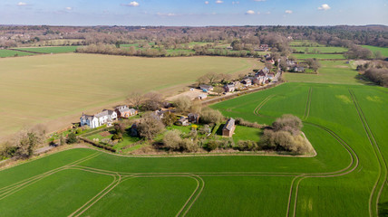 An aerial view of a scenic rural village in the middle of green fields under a majestic blue sky and white clouds