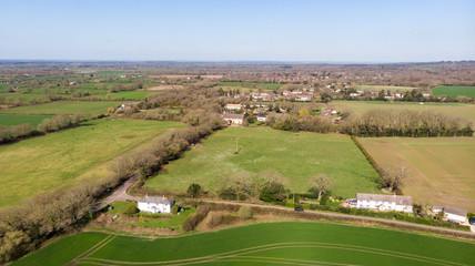 An aerial view of a scenic rural area with houses in the middle of green fields under a majestic blue sky
