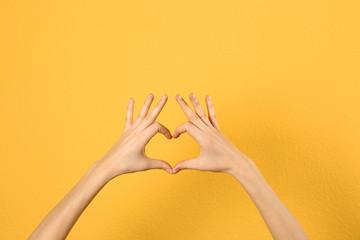 Woman making heart with her hands on color background, closeup