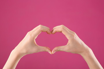 Woman making heart with her hands on color background, closeup