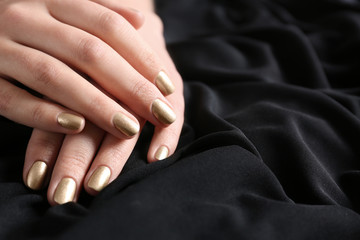 Woman showing gold manicure on black fabric, closeup with space for text. Nail polish trends