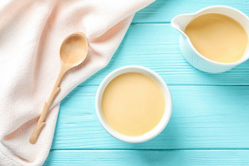Flat lay composition with bowl and jug of condensed milk on wooden background