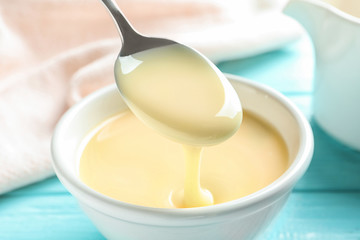 Spoon of pouring condensed milk over bowl on table, closeup. Dairy products