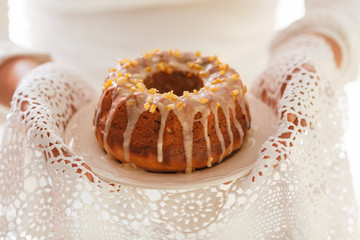 Easter Yeast cake on a white plate held by female hands, when served to the table. Traditional Easter cake with raisins and icing with candied orange peel