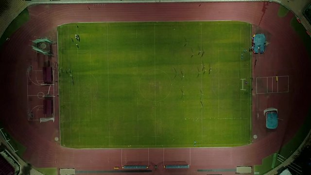 Aerial top view footballl players run on the footballl field. Vertical down shot, drone fly up drom players