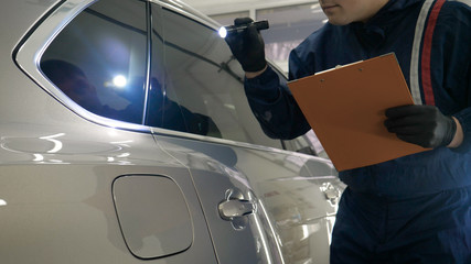 Slow Motion Man (Male) professional in working uniform and flashlight folder in his hands checks the car from all sides for serviceability Concept of: Car center, Service, Diagnostics.