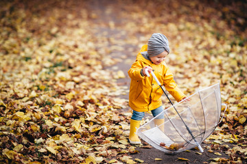 happy child girl with an umbrella and rubber boots in puddle on an autumn walk