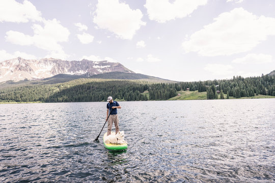 Man stand up paddleboarding  with dog with countains in the background Colorado