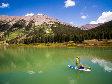 Couple paddling with their dog on paddle board at reservoir in mountains near Aspen, Colorado, USA