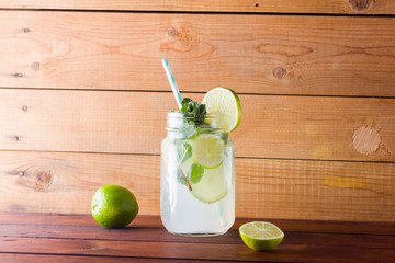 Mojito and mint on wooden background. Refreshing cocktail with lime and fresh mint on wooden boards. Two jars with handles with a summer drink with citrus and ice. Homemade mojito