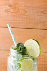 Mojito and mint on wooden background. Refreshing cocktail with lime and fresh mint on wooden boards. Two jars with handles with a summer drink with citrus and ice. Homemade mojito