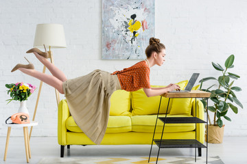 elegant young woman levitating in air and using laptop in living room