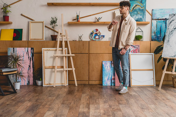 good-looking artist in pink shirt and blue jeans standing in spacious light gallery