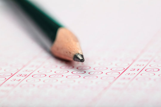 High School Or University Student Hands Taking Exams, Writing Examination On Paper Answer Sheet Optical Form Of Standardized Test On Desk Doing Final Exam In Classroom. Education Literacy Concept. 