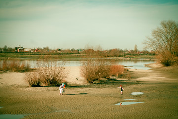two person man and woman in striped clothes go away a sandy wasteland with balloons and suitcase past the river
