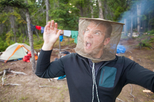 A Man Swats At Mosquitoes While Wearing A Mosquito Head Net At His Campsite.