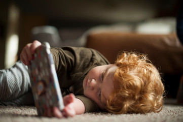 Toddler boy enjoys watching phone while laying on the floor