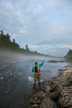 Fly fisherman casting into the foggy waters of teh Kennebec River, Maine