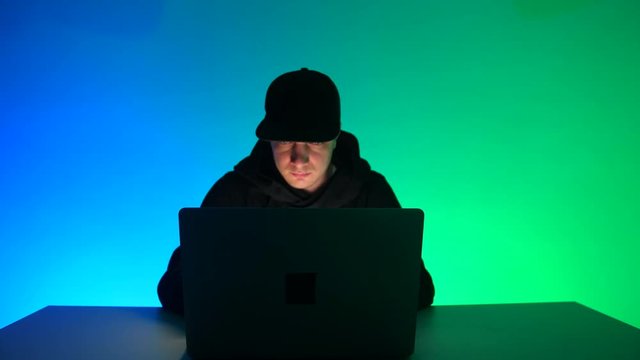 A young hacker in a black gown is working at a computer on a cyber attack in the office. Anonymous user commits cybercrime